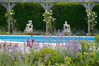 Swimming pool terrace for an older property with summer borders, oak pergola and feature statues, West Sussex