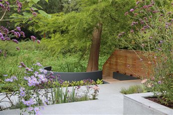 The River Garden in Hertfordshire. A terraced garden leads down to the river past colourful planted beds. A curved seat cantilevers out over the river  - a place to relax and unwind.