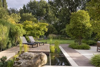 Timeless contemporary garden in Hertfordshire. Natural stone paving with clay pavers, formal pond with planting and decking, timber boardwalk leads through planting at the end of the garden to the river.