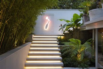 After dark in a London Courtyard Garden on two levels.  Sleek floating steps are lit from underneath lead from the basement to the upper garden. A light sculpture is the focal point.