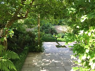 A small courtyard garden in Wilmslow has replaced with a small lawn with new stone paving, with two timber arches for wisteria to grow over.