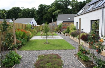 Village garden in Auldearn, near Nairn. An ornamental herb garden in raised timber planters sits alongside a granite sett seating area, with crab apples and perennial borders planted for pollinators.