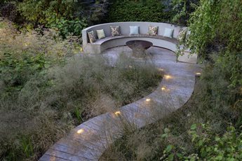 A hideaway at the end of a long garden, backing on to a river. The curved seating is nestled amongst willows and tall wild planting with a decked boardwalk snaking through the planting. 