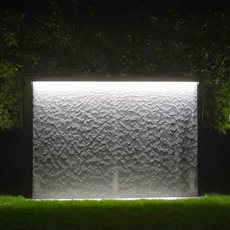 AquaVeil water wall illuminated at night. Integrated lighting brings the flowing water to life after dark, revealing changing patterns across the water surface and creating a striking focal point within the garden.