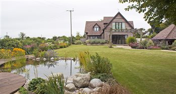 Naturalistic, creative design for contemporary timber-framed barn. Includes a large pond with a curved, cantilevered boardwalk, a naturalistic tiered water cascade with boulders and marginal aquatic planting, formal kitchen garden with fruit cages.