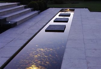 This sleek landscape 'canal' provides a stylish feature in this contemporary garden. The underwater lighting highlights the layer of black pebbles 