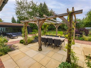 Oak pergola with scented climbers creating dappled shade over this courtyard dining area
