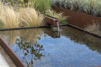 A corten steel water trough and spout adds drama and brings to sky down into he space in this contemporary country garden in Kent