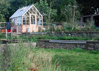 greenhouse with terraced gabion walls and wildflowers