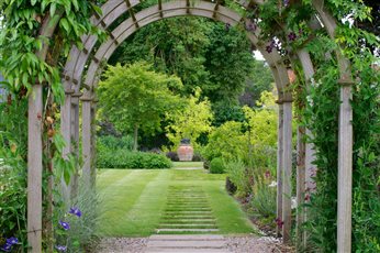 Elegant pergola leads to large pot focal point.  Continuing the stepping stones from the tunnel, through the grass to the pot emphasises the line.