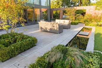 A Cheshire Garden. A large stone terrace was divided between a relaxed seating area and a dining area. A formal reflective pool was incorporated with a stepping stone across to the large lawn.