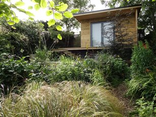 Cabin for nature watching set in naturalistic planting scheme on top of a difficult sloping garden.