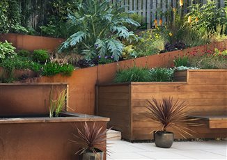 A steeply sloping triangular garden was remodelled with corten steel and cedar clad retaining walls. Light coloured paving brings light into the space
and rich coloured planting enhanced the colour scheme.