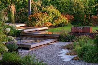 A contemporary, plant-filled garden for a suburban Glasgow new build property. Deep borders envelop the multi-layered deck and pergola. Close by the sound of running water soothes and propagates the scent of the roses. Photo credit: Swan Photography